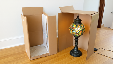 An unboxed handmade Turkish mosaic glass table lamp sitting next to its open shipping box on a wooden floor, ready to plug in