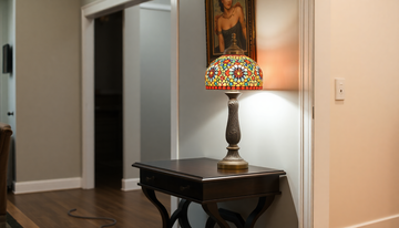 A handmade Turkish mosaic glass table lamp on a console table with its cord neatly routed along the baseboard toward a wall outlet