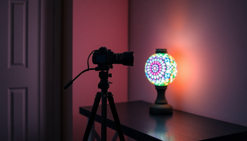 A hand-cut Turkish mosaic glass lamp glowing on a nightstand in a dim room, its colored glass pattern lit from within by a warm LED bulb