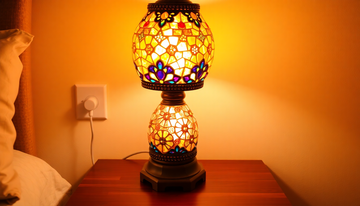 A handmade Turkish-style mosaic glass lamp glowing warmly while plugged into a US wall outlet