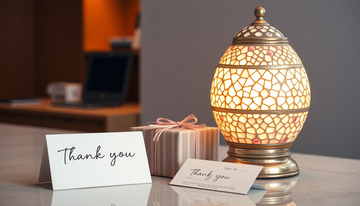 An elegant white and rose-toned Turkish mosaic glass lamp on an office desk beside a wrapped gift box and a thank-you card