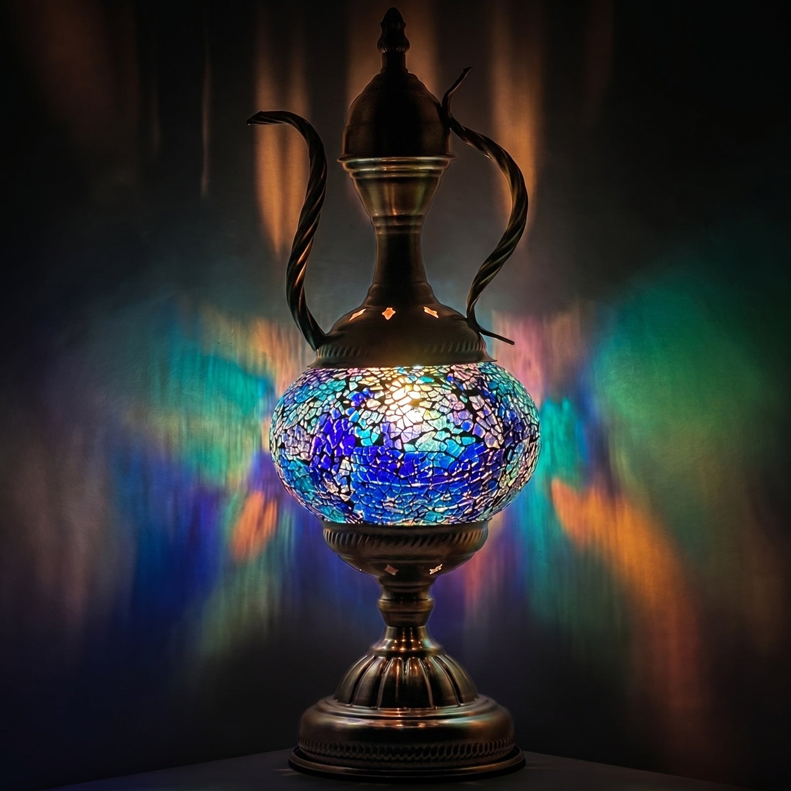Blue and amber mosaic glass ewer table lamp glowing warmly against a deep dark background