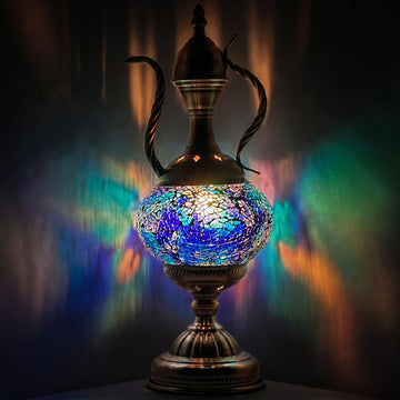 Blue and amber mosaic glass ewer table lamp glowing warmly against a deep dark background