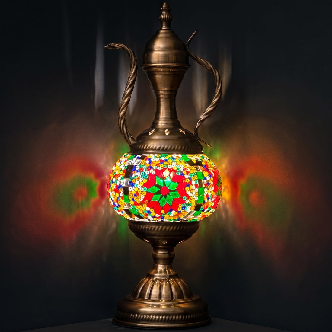 green vintage mosaic glass table lamp with an ornate pitcher-shaped body glowing softly against a dark background