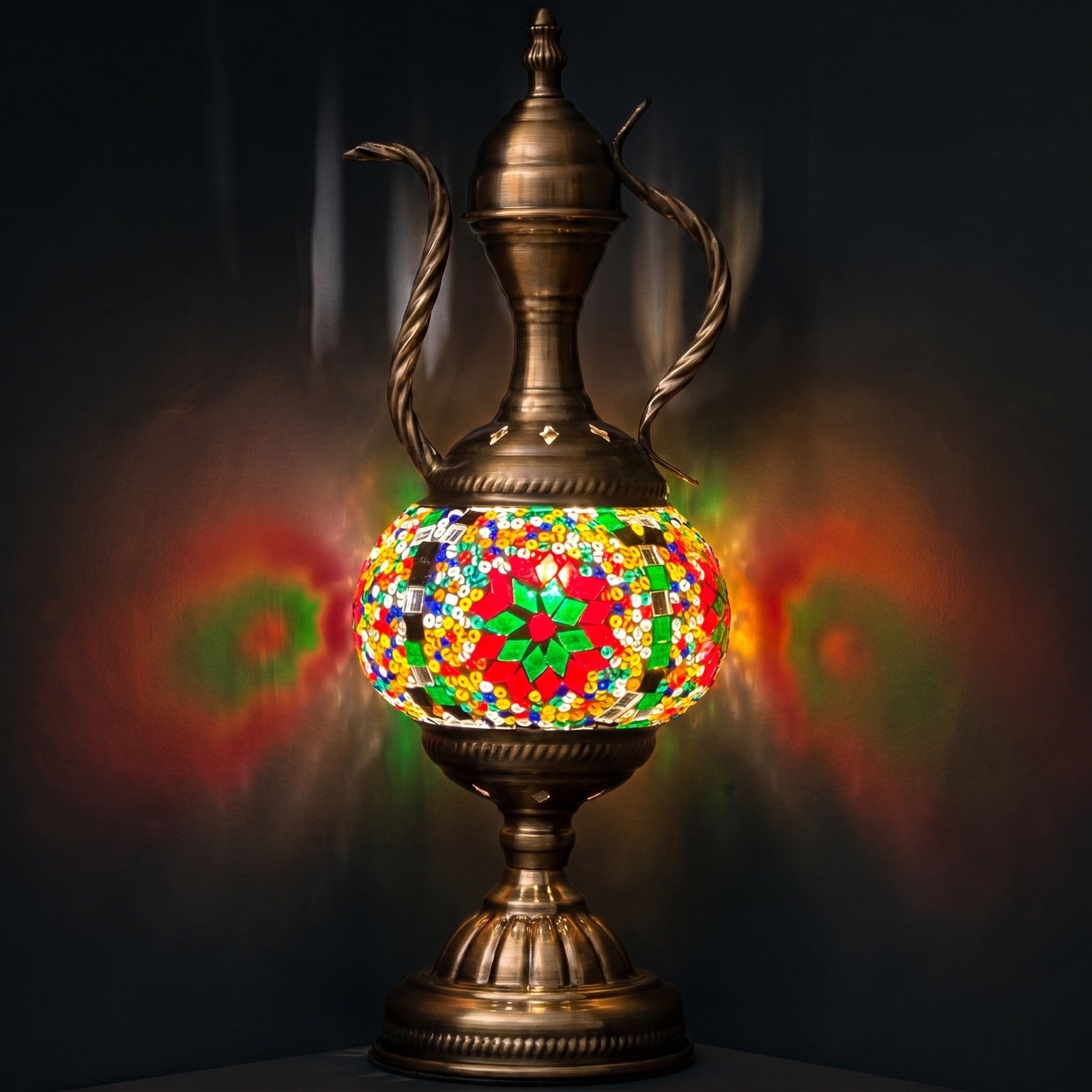 green vintage mosaic glass table lamp with an ornate pitcher-shaped body glowing softly against a dark background